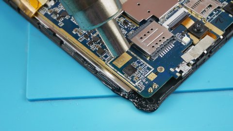 The repair of the smartphone.With a blow dryer to warm the chip on the chip.Repair the phone.Motherboard smartphone.Closeup.Repairman electronics soldering iron heats and removes the chip on the Board
