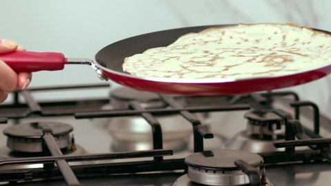 Slow-motion of a woman's hands flipping pancakes/french crepes in the air from a pan on the gas stove.