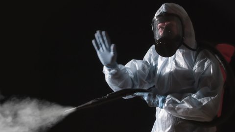 Caution Disinfection is in Progress. A man in a protective suit, glasses and a respirator sprays a disinfectant. At the same time, he makes gestures symbolizing the ban on presence