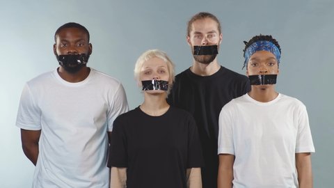 Portrait group of people with tape on mouth look at camera grey background silence gender freedom equality discrimination movement crisis citizen censorship international slow motion