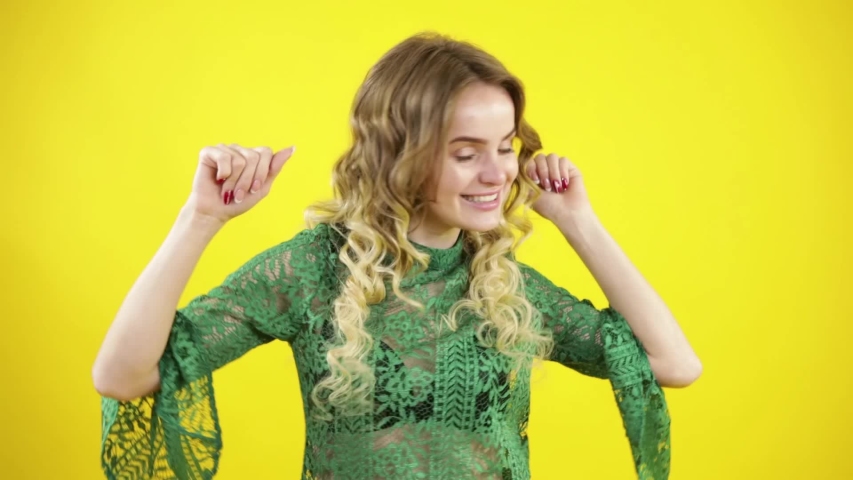 Attractive young girl dancing in front of a yellow wall while listening to music at a party
