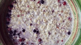 Cooking breeakfast at home.Oatmeal porridge with blueberry & raspberry berries filling with hot water shot directly from above in close up footage.Healthy lunch meal preparation 