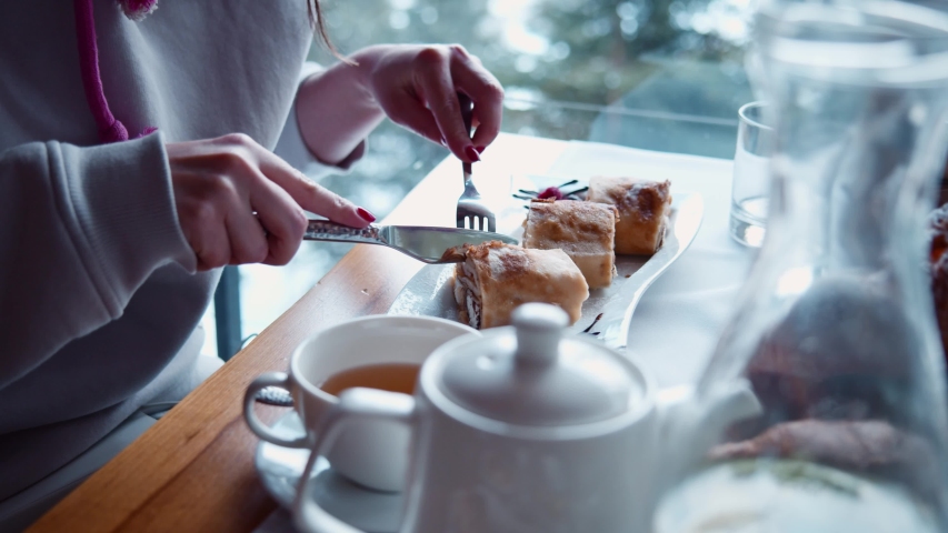 Young woman slicing and eating delicious baked pancakes in the cafe. Morning breakfast in continental restaurant. All inclusive resort hotel. Luxury lifestyle. | Shutterstock HD Video #1055087774