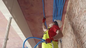 Mature plumber adjusting plastic tubes to ceiling on construction site. Foreman fixing plastic tubes for electrical wires in ceiling in wiring system on unfinished construction site