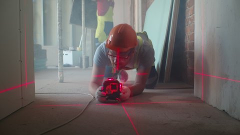 Professional worker using laser level in building on construction site. Construction worker installing and adjusting laser level on floor before measuring
