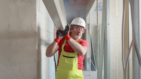 Portrait of two construction worker in protective goggles, helmet and uniform carrying pile of metal u channels for wall construction during house renovation