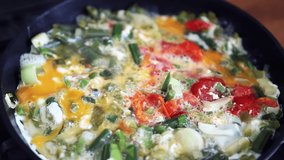 Traditional Italian frittata with chicken eggs & fresh vegetables frying on hot pan in home kitchen for healthy breakfast meal.Delicious stir fry cooking footage in close up