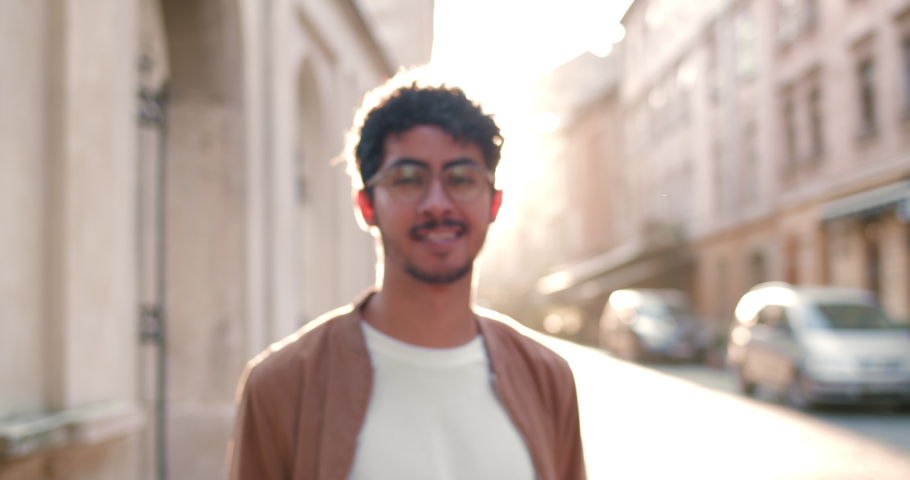 Crop view of millennial man in glasses looking to camera and smiling. Portrait of good looking guy with nose ring standing at old city street. Zoom in. Concept of people and real life. Royalty-Free Stock Footage #1055093411