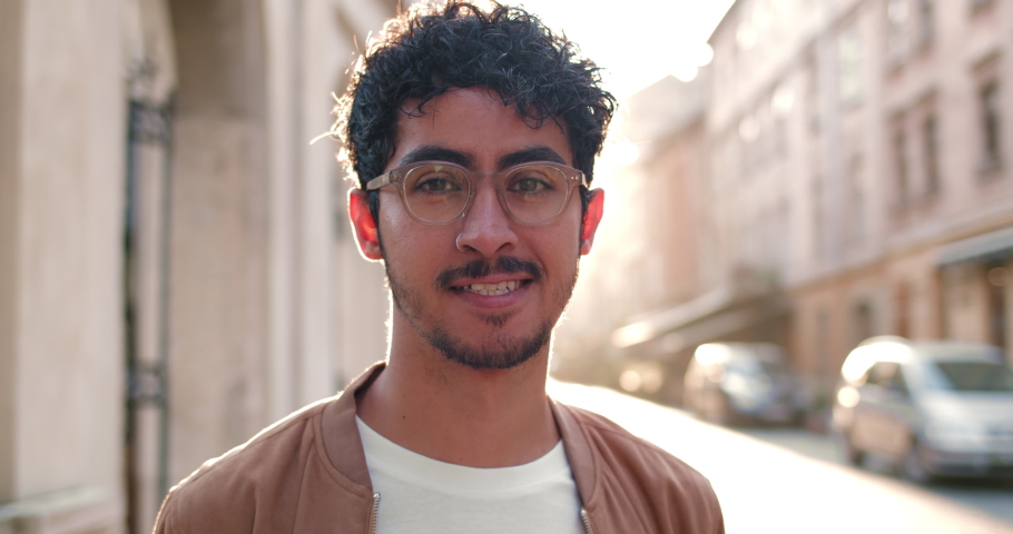 Crop view of millennial man in glasses looking to camera and smiling. Portrait of good looking guy with nose ring standing at old city street. Zoom in. Concept of people and real life.