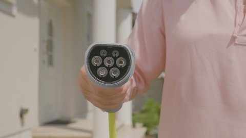 A woman covering the camera with a plug that charges electric cars