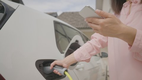A woman controlling the charging of her electric vehicle on her phone