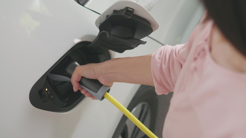 A woman opening the electric car's hatchet and plugging it in to charge Royalty-Free Stock Footage #1055094383
