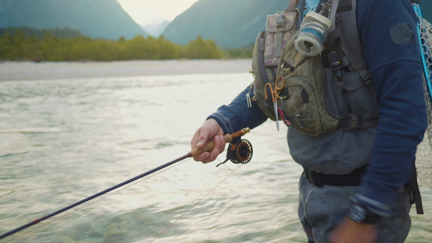 Shot of a fisherman, swinging the rod, who is standing in a river in the wilderness