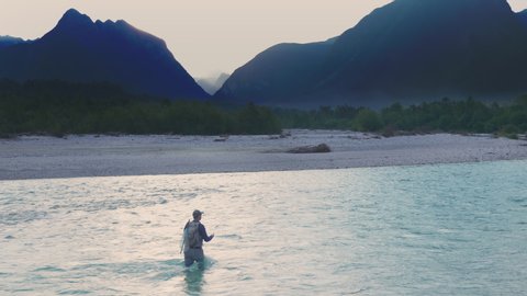 Drone shot of a man flyfishing in the turquoise river located in the wilderness. Filmed just before sunrise