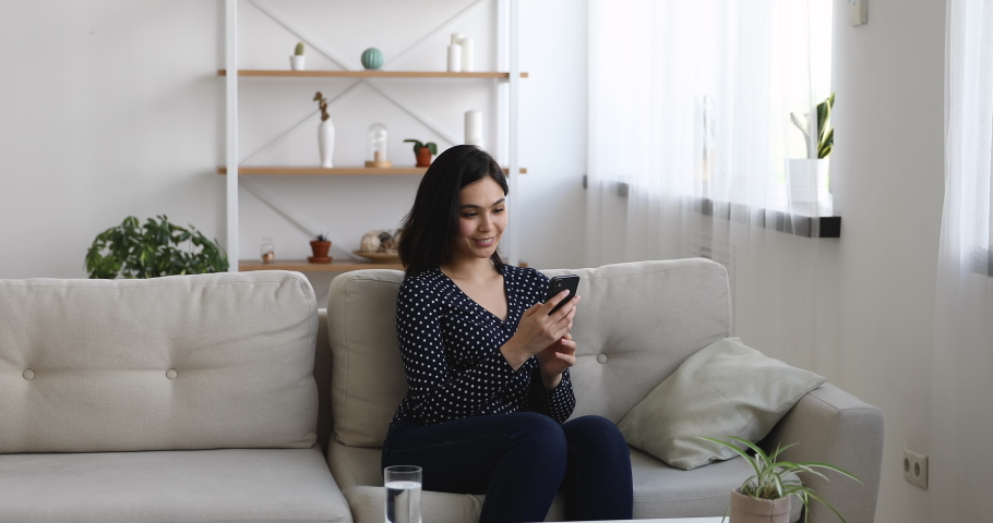 Vietnamese woman sit on sofa in living room hold smartphone received message stand up jumping feels excited looking very happy, opportunity new job of dream, got hired. Winner enjoy moment of victory Royalty-Free Stock Footage #1055094431