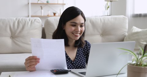 Happy asian woman sit at coffee table in living room manage household finances family budget make payments use laptop, calculate expenditures use calculator, do research, check home expenses concept