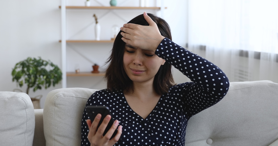 Asian woman sit on sofa hold cellphone read unpleasant news bad sms feels upset start crying. Bank notice about debt, student unsuccessful exam pass, not hired of dream job. Moment of failure concept Royalty-Free Stock Footage #1055094488