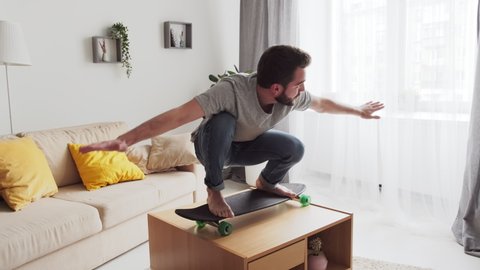 Modern man spending lockdown time at home practicing skateboard balancing on coffee table in living room