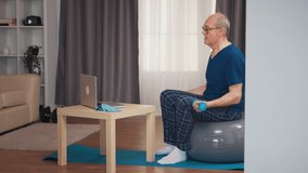 Senior man training in living room with dumbbells during online fitness program. Old person pensioner healthy training healthcare sport at home, exercising fitness activity at elderly age