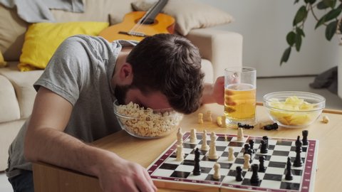 Funny footage of boozy bearded man waking up after falling asleep right in bowl full of popcorn in front of chess board