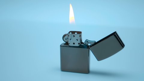 Fire burns in a metal zippo lighter standing on a white surface. Closeup. Rotation