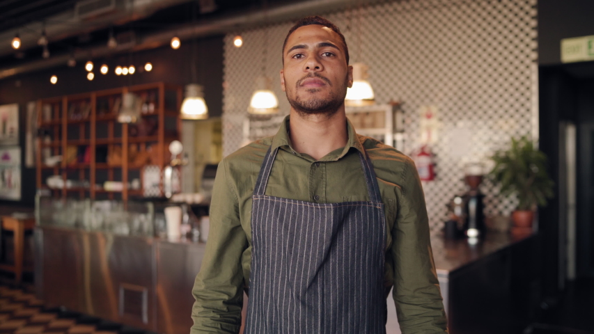 Portrait of successful african male chef wearing black apron standing with folded arms in cafe against counter Royalty-Free Stock Footage #1055098874
