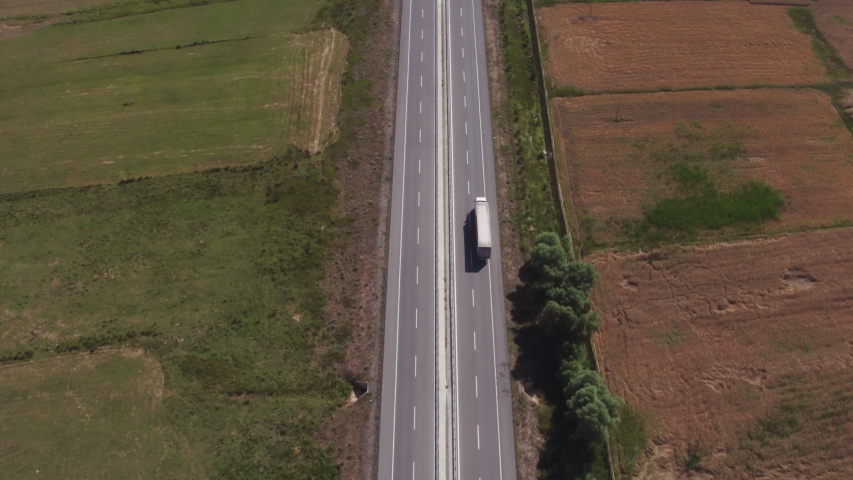 Semi truck alone driving on highway / White truck with trailer fast driving on straight autobahn among arid countryside flat dry landscape at summer sunny day / Aerial drone wide view Royalty-Free Stock Footage #1055099315