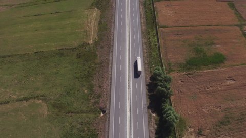Semi truck alone driving on highway / White truck with trailer fast driving on straight autobahn among arid countryside flat dry landscape at summer sunny day / Aerial drone wide view