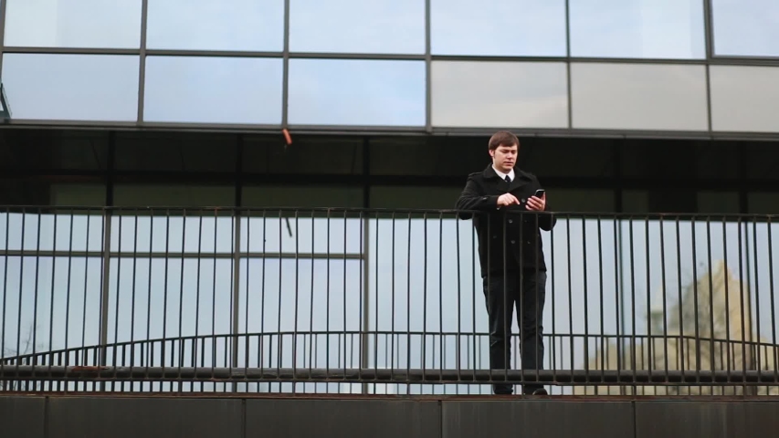 Businessman in a black coat talking on the phone against the background of the building