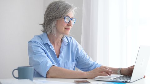 Mature lady in glasses using laptop, watching photos or reading morning news