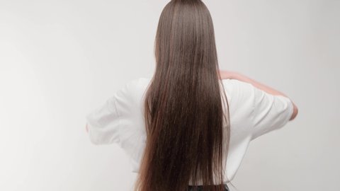 Close-up brunette developing hair in studio on a white background. Rear view of a girl with beautiful manicured hair.