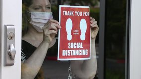Female shop owner wearing a face mask posts a notice on the glass door entrance requiring social distancing for entry - Powered by Shutterstock - Get 15% off with code: PIKWIZARD15