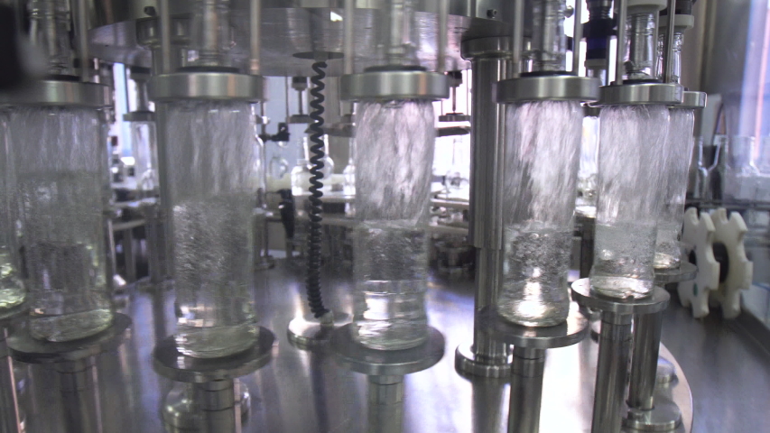 Factory for bottling alcohol. Working machine with conveyor line for production of alcoholic beverages. Glass bottles with vodka in conveyor belt in distillery production line. Royalty-Free Stock Footage #1055104238
