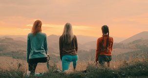 Group of sporty women practicing yoga pose together, stretching health on top of mountain in meadow at sunrise, zen wellness. Teamwork, good mood and healthy life concept. 4K slow motion video.