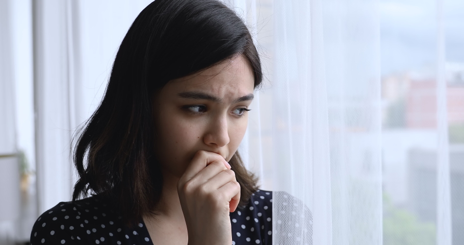 Close up view Vietnamese ethnicity young woman standing near window at home looking into distance outside waiting for beloved man feels cheated, hopes he will come. Female and break up divorce concept | Shutterstock HD Video #1055106494