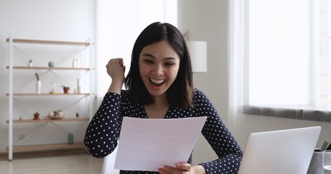Happy Asian woman sit at desk read letter about college admission, scholarship approved, invitation for internship abroad. Got hired job of dream, bank loan accepted, moment of celebration of victory