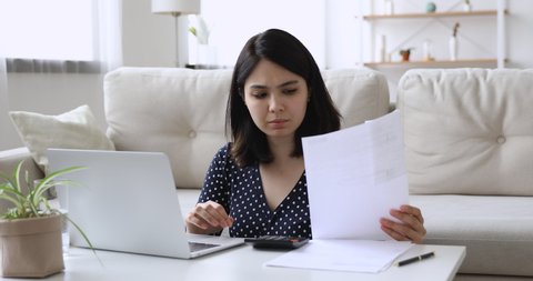Vietnamese woman sit at coffee table in living room holding paper checking domestic bills calculates data feels upset due high prices or debt. Lack of finances, financial problems, bankruptcy concept
