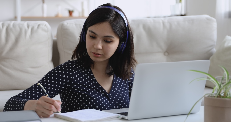 Focused asian woman in headphones using pc sit at coffee table at home, pretty student girl writes notes learn language, do task, watch on-line webinar, listen audio course, e-learn education concept Royalty-Free Stock Footage #1055106695