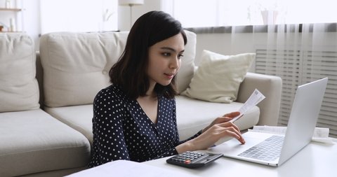 Asian woman small business owner sit at coffee table, check bills, incomes invoice count amount use calculator and pc application summarize data feels satisfied. Enough money, good work result concept