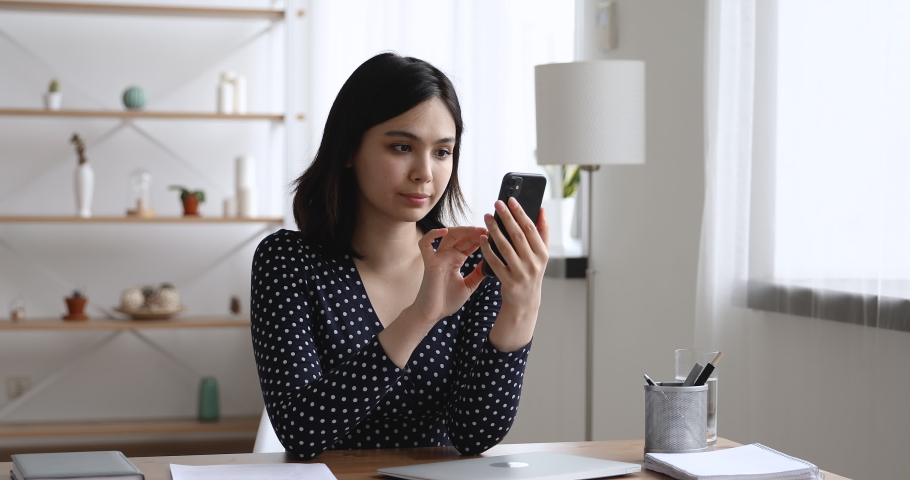 Asian woman sit at desk hold cellphone typing message receive sms from bank feels incredible happy. Girl makes yes I did it gesture look very excited. Achievement, got hired, lottery money win concept Royalty-Free Stock Footage #1055106719