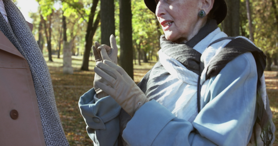 Portrait of admiring elderly woman talks pleasantly to her man, remembers something and smiles under the sunny sky in autumn park. Slowly in 4K