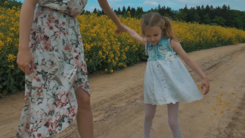 Cheerful happy pretty young mother with adorable little daughter having fun, dancing, enjoying leisure on yellow flower field in the countryside. Motherhood and childhood