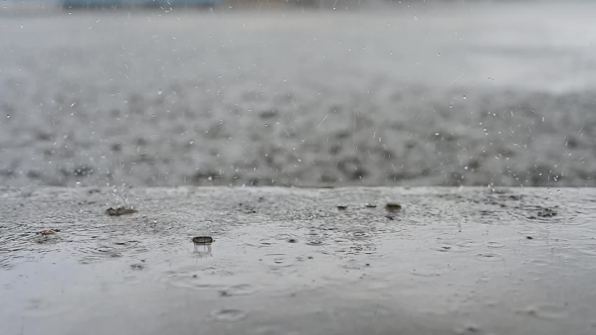 Slow Motion, rain water drops falling into big puddle on asphalt, flooding the street. Road floods due to the heavy rain in wet season. Raindrops falling down