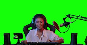 Young beautiful asian streamer vlogger wearing headphones have fun dancing in her live broadcasting on a computer with colourful UV lighting over green screen background. POV monitor screen view.