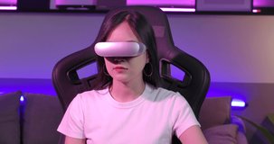 Excited young asian teen gamer wearing virtual reality glasses and holding controllers having fun enjoy playing motion sensing interaction vr game in colourful UV lighting living room at home. 