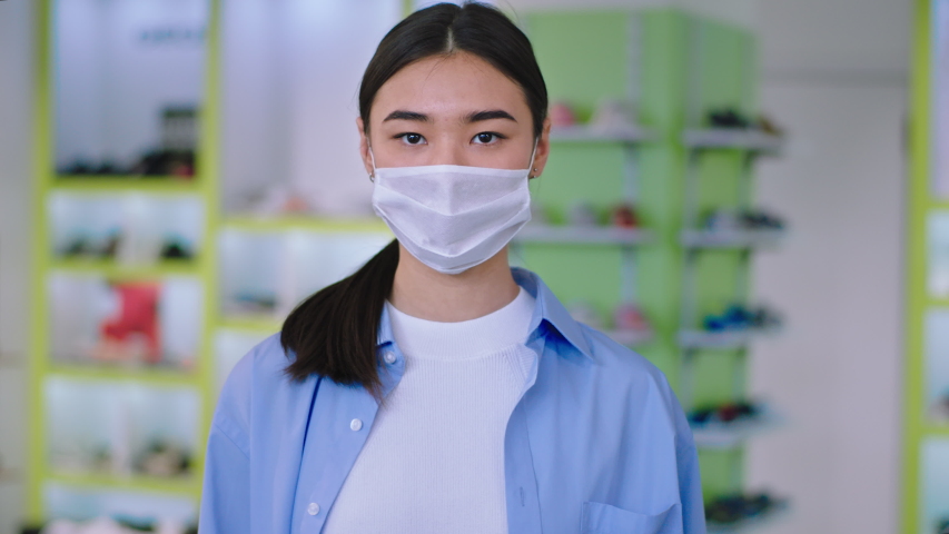 Asian young woman with a protective mask portrait looking straight to the camera concentrated she is in a shop. 4k