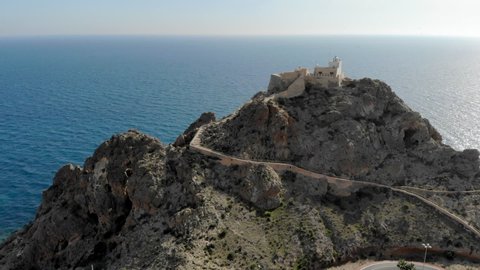 Cabo de Gata old lighthouse located on rocky mountain top. Aerial footage drone point of view beacon surrounded by Mediterranean Sea flock of flying birds idyllic nature scenery. Almeria España, Spain