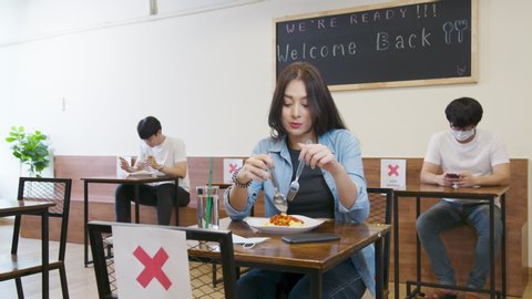 Arrangement blank space table to prevent and stop coronavirus spread by social distancing concept. Asian woman and asia people eating food alone at table in reopening restaurant after lockdown measure