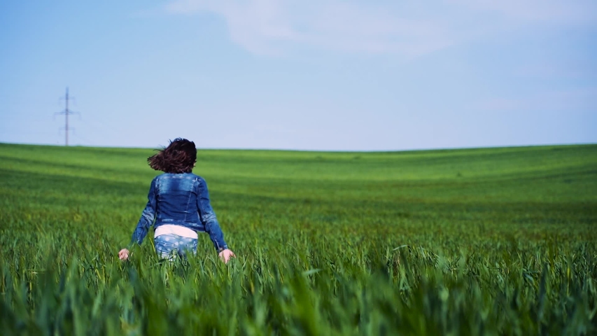 Girl runs across the field. Green wheat and blue sky as a background