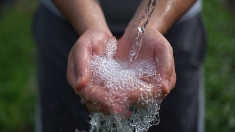 stream of fresh drinking water pouring into human hands, dry farmland, lack of water. Clean water splashing on hands of the poor rural man in a drought affected area